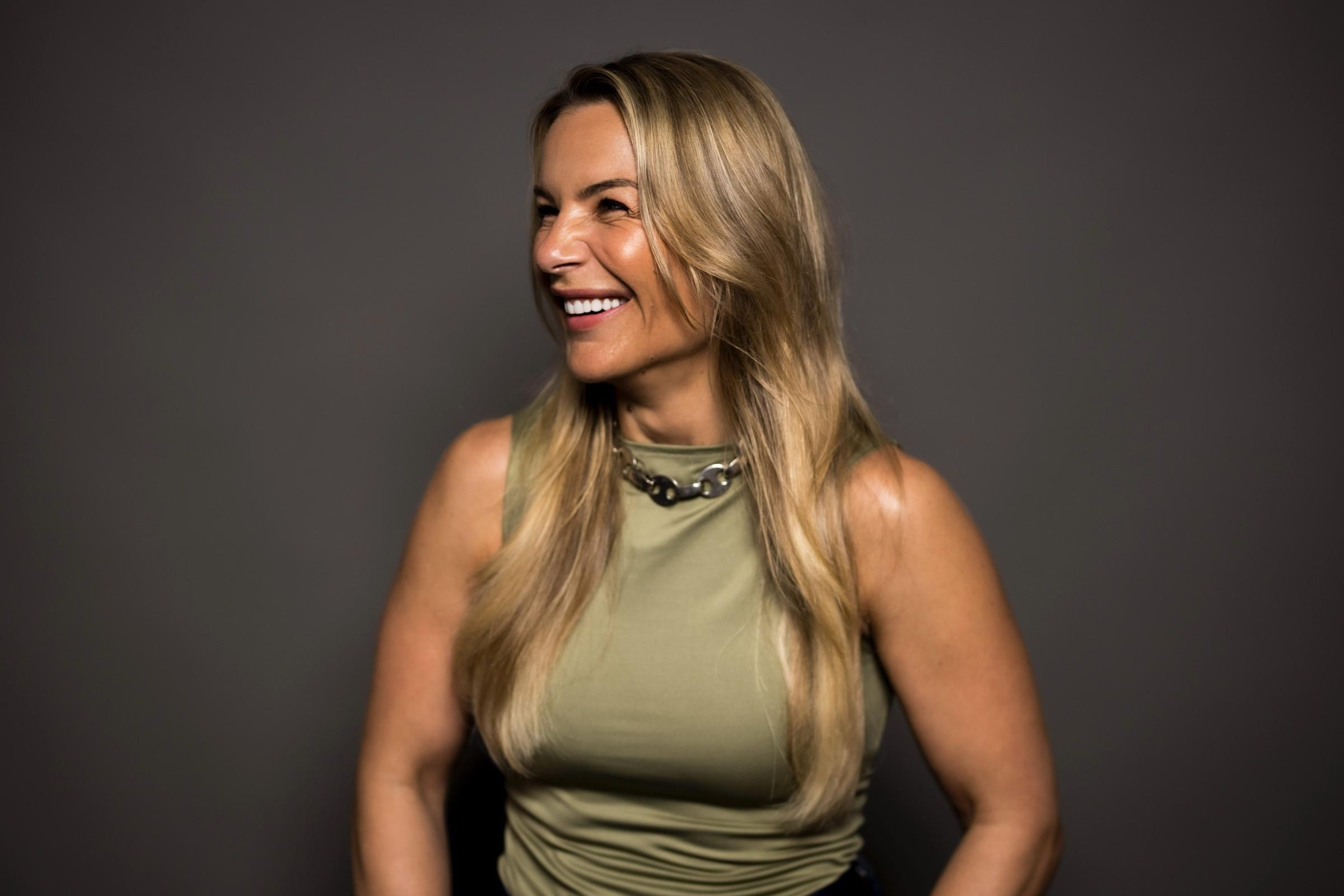 Zoe Kapsalis laughing in a studio portrait, olive top against a charcoal backdrop